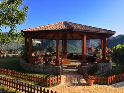 a wooden gazebo with a table and flowers at Rooms Dujeva Drago-Resort in Rijeka Crnojevića