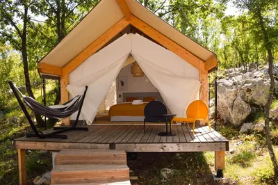 a tent with a bed and a hammock on a wooden deck at Oblun Eco Resort - New Glamping Tents near Lake Skadar in Podgorica