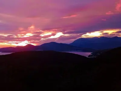 a sunset over mountains and a body of water at Apartman u sumi nedaleko od mora in Bigovo
