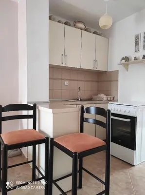 a kitchen with white cabinets and two chairs in it at Apartman u sumi nedaleko od mora in Bigovo