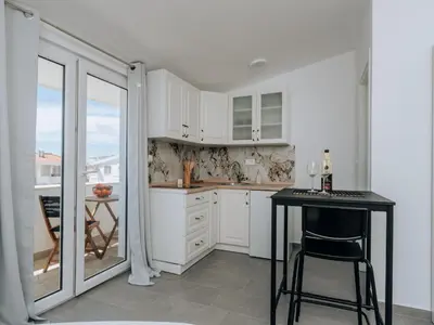 a kitchen with white cabinets and a table and a balcony at Apartments Milivojevic in Bar