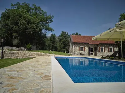a swimming pool with an umbrella and a house at Holiday home Zlatna Glavica in Podgorica