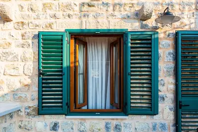 a window with green shutters on a stone building at Boutique hotel Ruzmarin SPA & Garden by Aycon in Budva