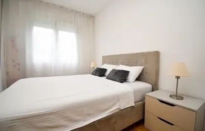 a white bedroom with a large bed and a window at Comfort Residence Art Zone in Podgorica