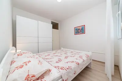 a white bedroom with a white bed with red sheets at Apartment Simanic in Budva