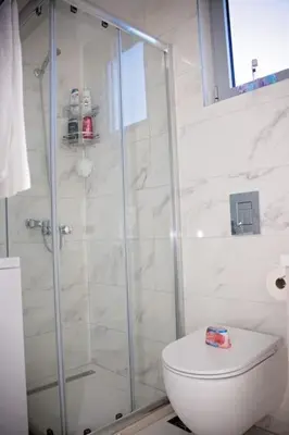 a white bathroom with a shower and a toilet at Sea view dobra voda in Dobra Voda