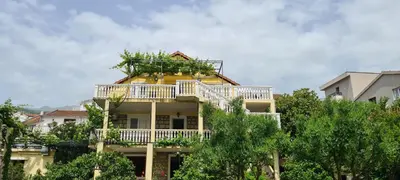 a yellow building with a balcony and trees at Guest House Andrea in Budva