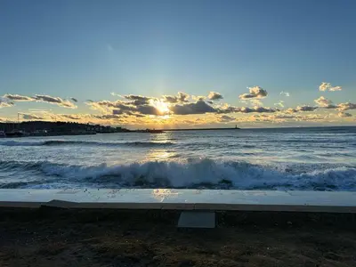 a sunset over the ocean with a bench on the beach at Light Bar Apartment in Bar