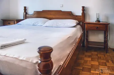 a wooden bed with white sheets and a wooden night stand at Vera Apartments in Budva