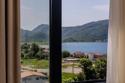 a window with a view of a lake and mountains at Hotel AQUILO in Petrovac na Moru