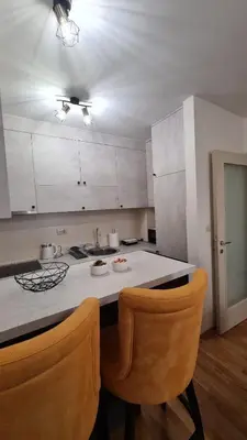 a kitchen with white cabinets and a counter with two chairs at Mara's cozy apartment in Podgorica