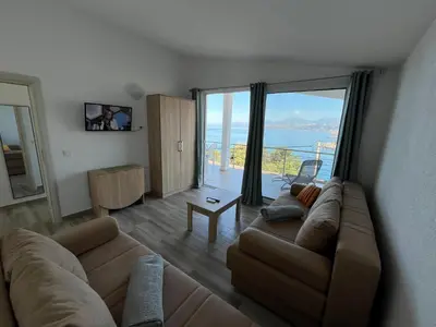 a living room with a couch and a large window at Jakovljevic apartman in Utjeha