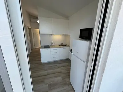 a small kitchen with white cabinets and a refrigerator at Jakovljevic apartman in Utjeha