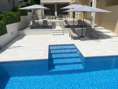 a blue swimming pool with chairs and umbrellas at Luxury Kotor bay view studio in Muo