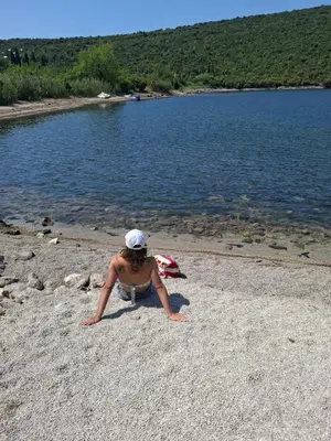 a woman sitting on the shore of a lake at Apartman u zelenilu Bigove in Kotor