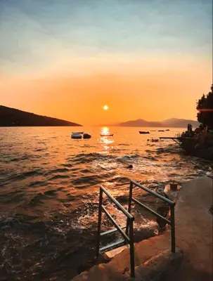 a bench sitting on the shore of a body of water at Apartman u zelenilu Bigove in Kotor