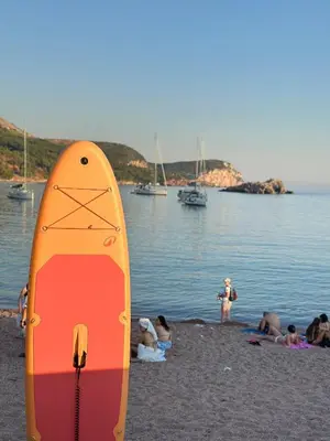 a surfboard on a beach with people on the water at Suite Apartment Sveti Stefan in Sveti Stefan