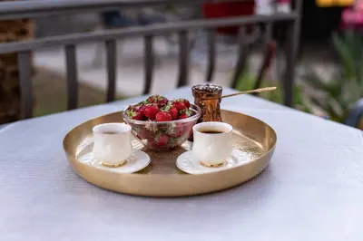 a tray with a bowl of strawberries and two cups of coffee at Apartmani Kaan in Podgorica