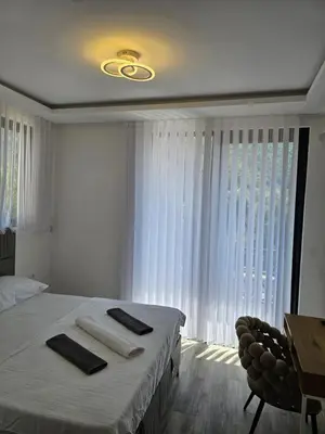 a white bedroom with a bed and a window at La Vida Apartments in Babalonija