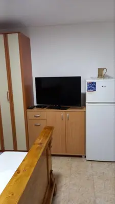 a room with a tv and a table and a refrigerator at Milica, Soba sa kupatilom in Petrovac na Moru