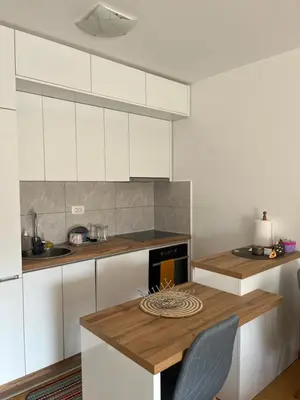 a kitchen with white cabinets and a wooden table at Marelica Apartman in Bar