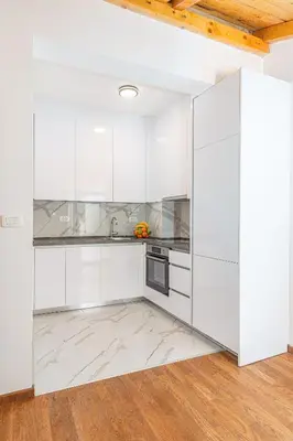 a white kitchen with white cabinets and a wooden floor at Adriatic Residence in Budva