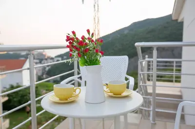 a table with two cups and a vase with flowers on a balcony at Vila Varagic in Budva