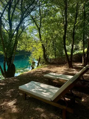 a picnic table and a bench next to a lake at Zeta River Glamping in Danilovgrad