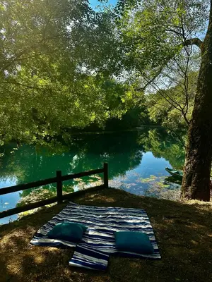 a mattress on the grass next to a lake at Zeta River Glamping in Danilovgrad