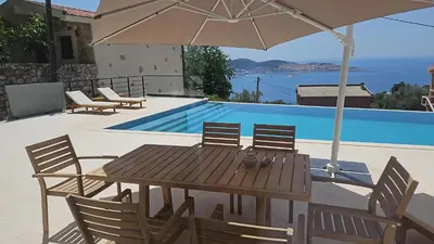 a wooden table with chairs and an umbrella next to a pool at Villa Infinity Bar Montenegro in Brca