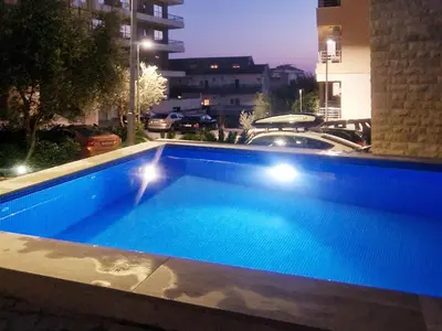 a blue swimming pool at night with a parking lot at Studio Apartment Ljilja in Budva