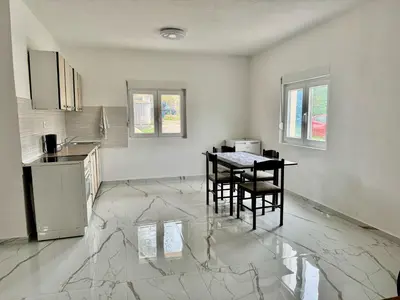 a kitchen with a table and chairs on a marble floor at Apartmani Gusani in Radanovići