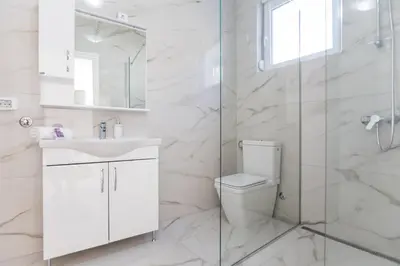 a white bathroom with a toilet and a glass shower at Villa Hanna Apartments in Sutomore