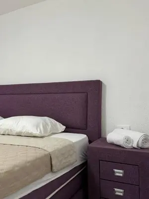 a bed with a purple headboard next to a nightstand at Apartment Airport DD in Mitrovići