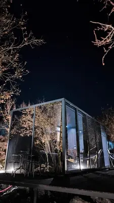 a glass building with tables and chairs at night at Oblun Eco Resort - Mirror Cabin in Podgorica