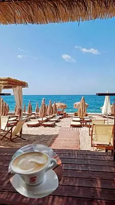 a cup of coffee sitting on a table next to a beach at Šušanj Bar in Bar, Susanj