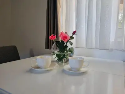 a table with two cups and a vase of flowers at Apartment Matija Airport in Podgorica