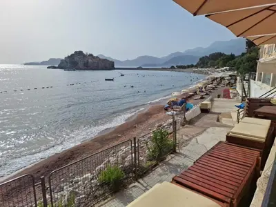 a beach with benches and umbrellas next to the water at Montesan Luxury Apartments Sveti Stefan in Sveti Stefan