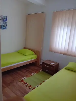 two beds in a room with green sheets and a table at Dara Apartmani in Donji Štoj