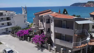 a building with purple flowers in front of the ocean at Apartments Abramovic in Sutomore