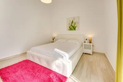 a white bed in a white bedroom with a pink rug at Sky Fort Apartment in Dobra Voda