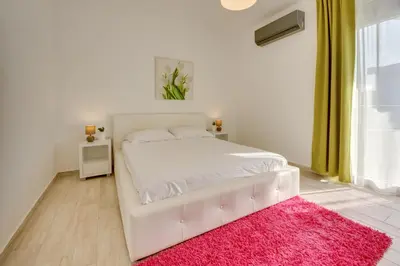 a white bed with a pink rug in a bedroom at Sky Fort Apartment in Dobra Voda