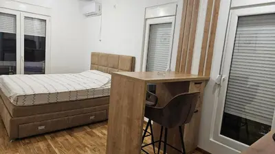 a bedroom with a bed and a desk and windows at Lamela B in Podgorica