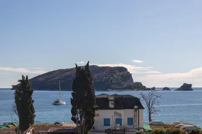 a house in front of a body of water with a boat at Tre canne cozy sea view apartment in Budva
