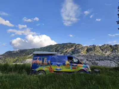 a colorful van parked in a field with a mountain at Escape Montenegro Campervan Tranzit in Podgorica