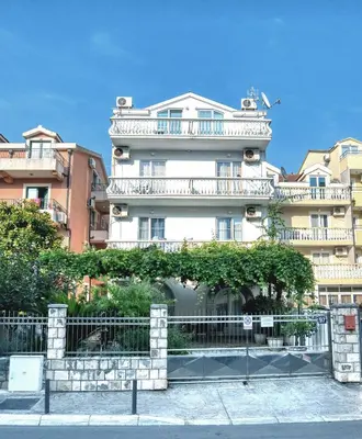 a tall white building with a fence in front of it at Sun Guest House in Budva
