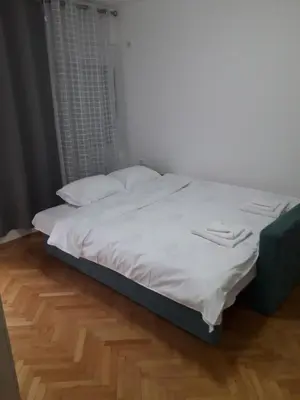 a bed with white sheets and white pillows on it at Apartman Autobuska in Podgorica