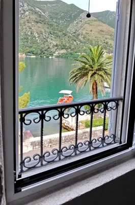 a window with a view of a lake and a palm tree at Apartments Ave R in Kotor