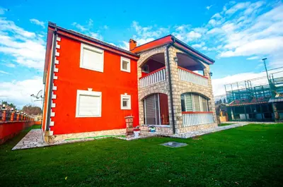 a red house with a green yard next to a ballpark at Milic Apartmant with parking in Bar
