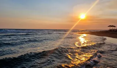 a sunset on a beach with the ocean at comjun in Ada